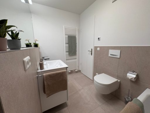 Heller, moderner Badezimmer mit Waschbecken, Toilette und Handtuchhalter.