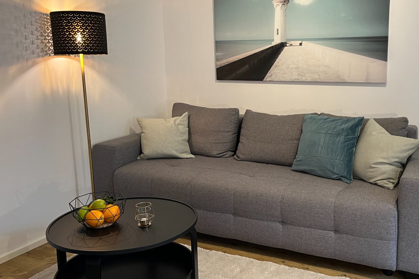 dekoriertes Wohnzimmer mit Sofa, Kissen, Bild an der Wand, elegante Stehlampe und einem Couchtisch mit Obstkorb