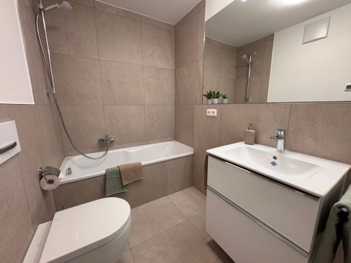 Modernes Badezimmer mit Badewanne, Waschbecken und WC in heller, neutraler Farbgestaltung.