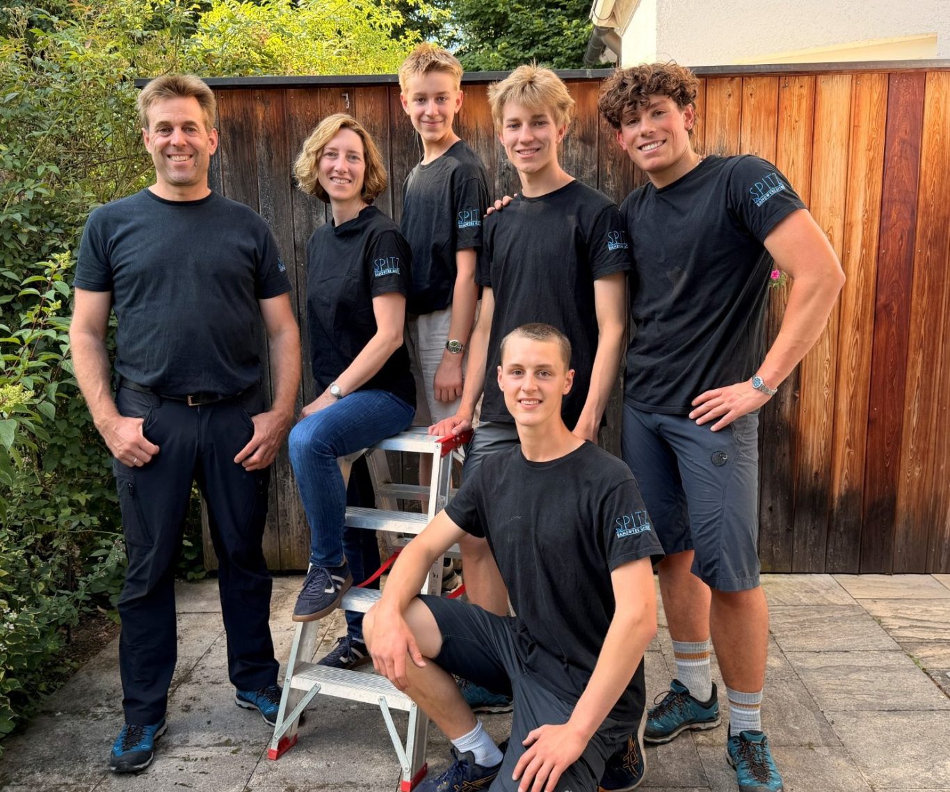 Das Team das Team: Vier Personen in schwarzen T-Shirts stehen in einem Garten mit grüner Umgebung.