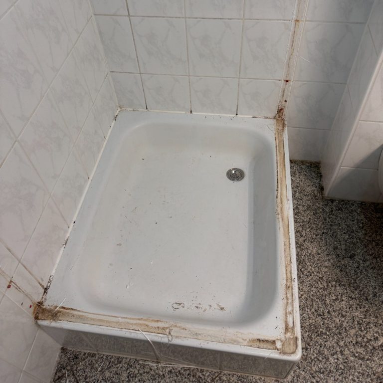 Duschtasse ohne Wände mit sichtbaren Abnutzungsspuren und Schmutz entlang der Kanten.