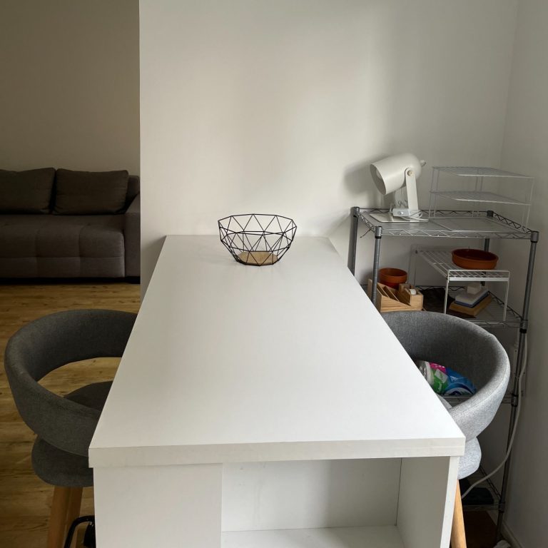 Minimalistischer Essbereich, kale Wände, mit einem schmalen weißen Tisch und zwei grauen Hochstühlen.