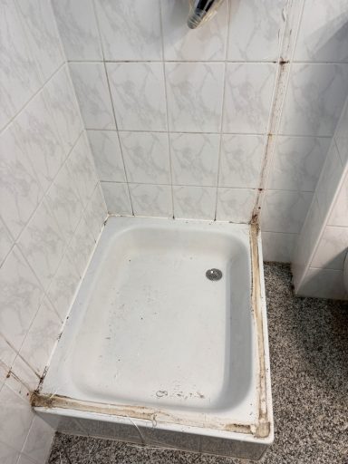 Duschwanne mit sichtbaren Schmutz- und Wasserflecken in einem Badezimmer.